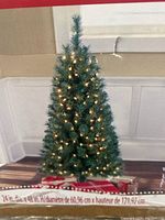 Front view of the four foot artificial Franklin Pine Christmas tree lit with white lights, placed on a wooden floor against a wall.