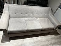 Front view of the grey couch showing three seat cushions and tufted backrest with slight fabric wear.