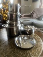 Stacked stainless steel pots and a saucepan with two lids on a table in living room setting, showing the full lot of pots and lids as per seller's description.