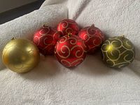 Six large Christmas balls in red, olive green, and gold with swirl decorations shown together on a soft surface.