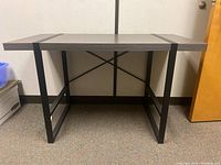 Front view of desk showing black metal legs and fabricated wood-look top with two black metal strips.