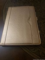 Front exterior of the closed tablet cover showing the gold synthetic leather finish with stitching detail and embossed logo