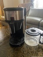 Full view of Tim Hortons branded Bunn coffee maker with separate glass carafe on a decorative surface in front of a gray couch.