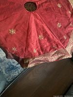 Full view of the circular red Christmas tree skirt laid flat showing gold snowflake embroidery and decorative edge trim