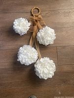 Overview of the four white fabric flower pom-poms detached on wooden floor with ribbon laid out, showing size and arrangement.