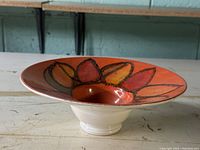 Side angle view of Poole Pottery bowl showing flared shape and floral decoration on orange background with white base.