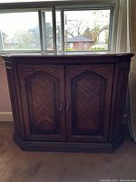 Front view of wooden cupboard with double paneled doors and metal handles