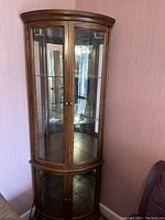Curio cabinet closed showing wood frame, glass doors, and curved top design.