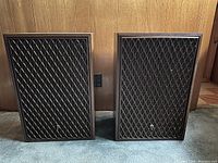 Pair of vintage wooden speakers with diamond lattice front grills shown side by side on floor.