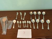 Full view of the Birks Regency silverplate utensil set laid out on a wooden surface including large spoons, small spoons, spreading utensils, and a carving set.