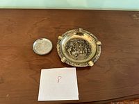Photo showing the brass ashtray and small silver-tone coaster on a wooden table
