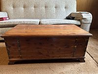 Closed view of cedar trunk chest showing wood grain, metal hinges, corner reinforcements, and base cut-out design.