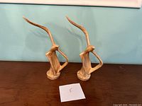 Pair of tall ceramic bird sculptures displayed side by side on a wooden surface against a light blue wall, showing their stylized elongated necks and textured glaze.