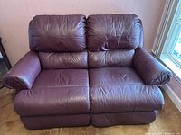 Front view of brown leather reclining love seat showing slight wear and creasing on cushions and armrests.