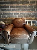 Front view of brown leather armchair with visible rolled arms and embossed golfer design on backrest.