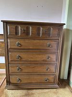 Front view of a vintage wooden dresser showing five drawers with metal ring pulls and detailed paneling.