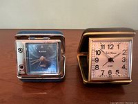 Front view of the Bulova and Seth Thomas vintage travel clocks side by side showing clock faces and cases partially open.