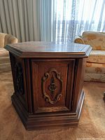 Hexagonal wooden end table showing carved panel and metal ring pull, richly stained wood finish.