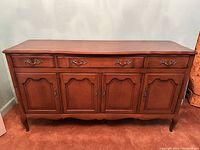 Full front view of vintage wooden cabinet showing four drawers on top and four paneled doors below with brass hardware.