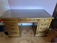 Full view of vintage wooden office desk with glass top, showing six drawers and kneehole.