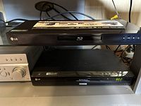 Front view of LG Blu-ray Disc/DVD player on top shelf with visible controls and disc tray.