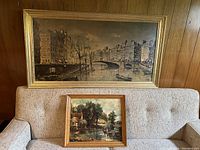 Both prints displayed together on a beige couch against wooden paneling, showing scale and framing