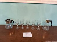 Full set of two glass coffee/tea pots and six matching etched glass cups displayed on a wooden surface.