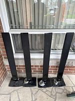 Four black LG tower speakers placed in front of a window on tile floor, showing front and side views, with visible wiring wrapped on base of three speakers.