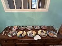 Wide view of all 10 decorative collectible plates arranged on a wooden surface beneath a mirror.