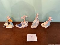 Four ceramic figurines arranged side by side on a wooden surface against a green wall.