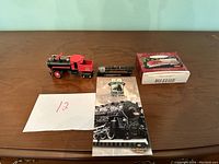 Photo showing four items: a red and black steam engine model train, black diesel locomotive model train, Hallmark Great American Railways Fall 1995 catalog, and a boxed model train named 'The Polar Express Pull Back Train'.