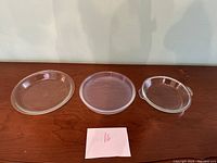 Set of three vintage clear plastic pie holders arranged side by side on wood surface, varying sizes visible.