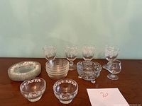 Overview of lot contents showing plates, bowls, stemmed glasses, and small cut glass bowl arranged on table.