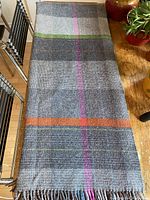 Full length view of the folded lambswool blanket showing grey checkered pattern with colorful stripes and fringed edge.