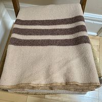 Folded wool blanket showing pale tea color with three chocolate stripes on one end and original blanket stitch edge.