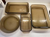 Full set of four vintage smoky brown glass ovenware pieces on a white surface.