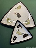 Overall view of both triangular plates, white background, black borders, decorated with textured green and brown leaf motifs