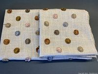 Folded cream linen blend fabric with multicolor embroidered circular dots in shades of brown, blue, olive green, and coral.