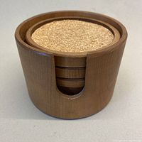 Round seamless maple wood container holding four round cork-lined wooden coasters, top view shows coaster cork surfaces flush with wood edges.