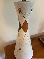 Close-up of off-white ceramic lamp base with speckled finish and harlequin pattern in brown and brass tones.