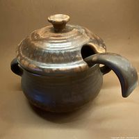 Side view showing the curved handle of the hand made ceramic casserole pot with lid and ladle slot.