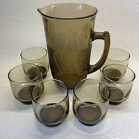 Front view of the smoky brown textured pitcher with handle surrounded by six matching stackable glasses, all set on a white surface.