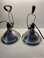 Two vintage metal clamp lamps showing metal conical shades with linear grooves and clamp handles on top.