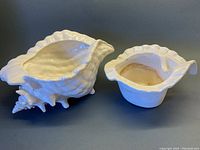 Two white ceramic pieces shaped like a conch shell, placed side by side showing the separate parts
