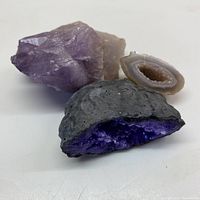 Photo showing three rocks: one raw light purple amethyst rock, one gray rock with sparkling dark purple interior, and one light gray polished slice with crystalline interior