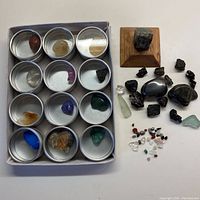 Overview of rocks in round metal containers and additional loose stones arranged on surface, including mounted stone display