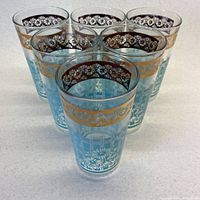 Set of six turquoise and gold vintage tumblers arranged in a row showing decorative floral designs