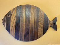 Fish shaped wooden trivet with striped wood pattern and inlaid circular eye detail.