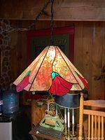 Hexagonal stained glass hanging lamp lit, showing mottled green and burgundy background with cherry red floral detail on each side, hanging by a black chain.