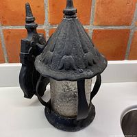 Full view of vintage black wrought iron wall-mounted light fixture with textured glass globe inside iron frame.